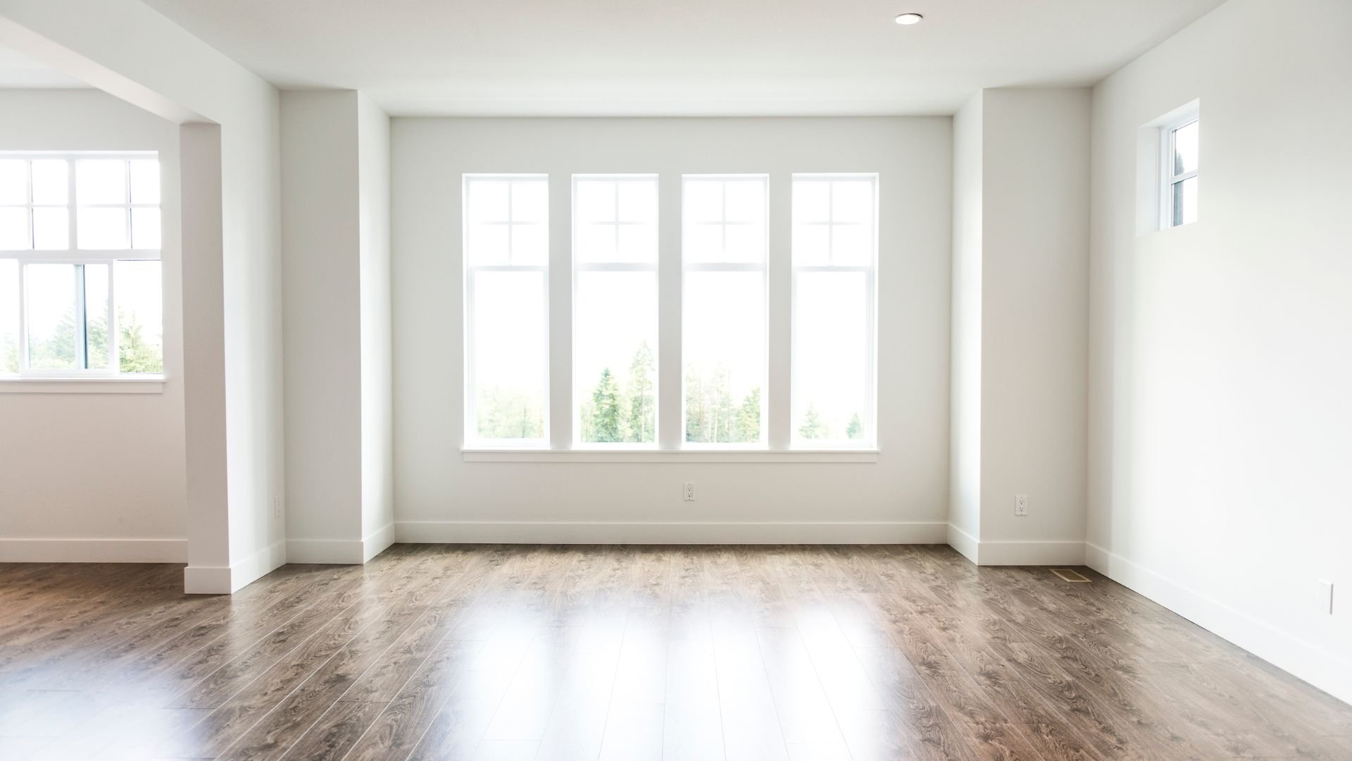 Empty white room with large windows and wooden floor, natural light